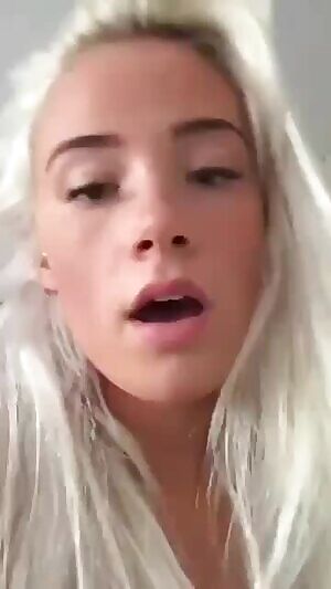 A blonde attractive woman is naked and having the sex from behind with presumably a man's penis via penetration to her vagina, all the while recording the scene with her cellular device. She is breathing rhythmically as the sound of the presumable man's testicles hits her labia major.